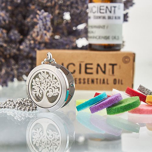 Silver tree-shaped locket with colorful soap bars and a bottle of essential oil in the background.
