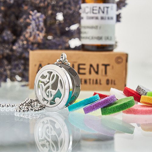 Silver locket necklace with colorful charms on a reflective surface, with a bottle of essential oil in the background.