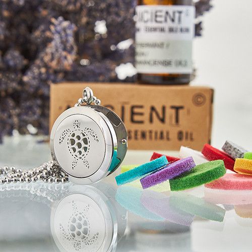 Silver turtle pendant necklace with colorful charms on a reflective surface, with a bottle of essential oil in the background.