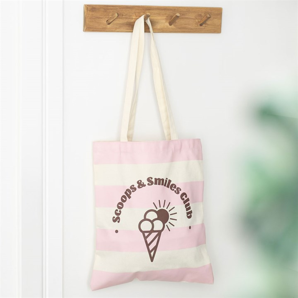 Tote bag with 'Scoops & Smiles Club' design hanging on a wooden hook.